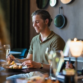 Man aan een tafel met eten, glazen en een tafellamp.